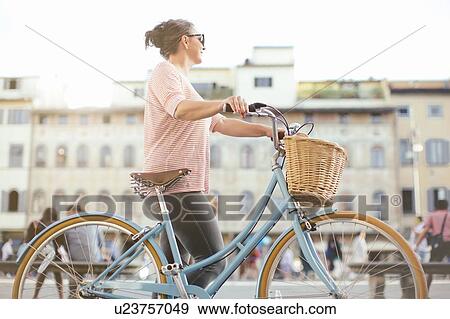 Side view of mid adult woman holding bicycle looking away View Large Photo Image Stock Photo - Side view of mid adult woman holding bicycle looking away. Fotosearch