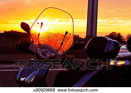 Stock Photo - Silhouetted moped parked on roadside at sunset. Fotosearch