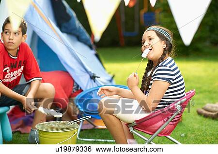 Stock Photograph - Sister and brother toasting marshmallows in front of homemade tent in garden. Fotosearch