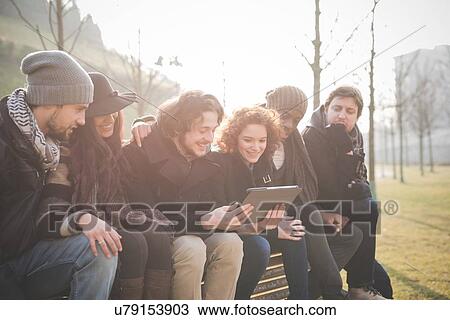 Six young adult friends reading digital tablet on park bench View Large Photo Image Stock Image - Six young adult friends reading digital tablet on park bench. Fotosearch