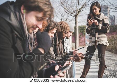 Six young adult friends using smartphones and digital tablets in park View Large Photo Image Stock Image - Six young adult friends using smartphones and digital tablets in park. Fotosearch