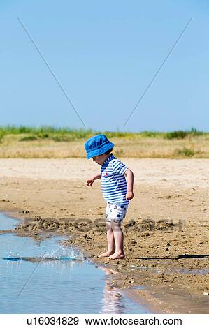Stock Photo - Small boy on beach throwing sand into sea, Marennes, Charente-Maritime, France. Fotosearch