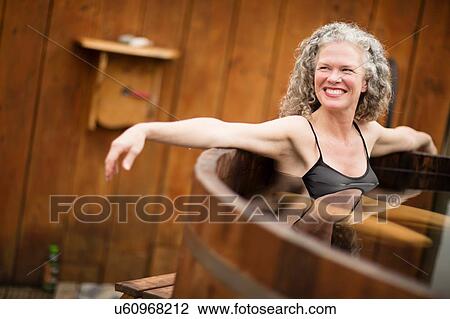 Stock Image - Smiling mature woman in hot tub at eco retreat. Fotosearch