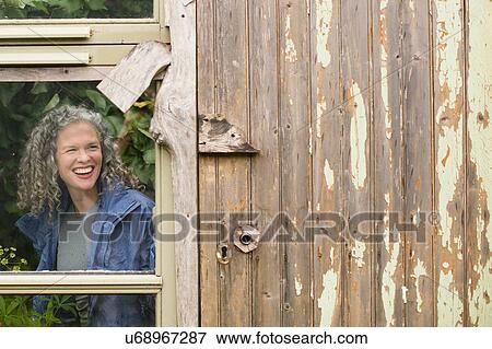 Smiling mature woman looking out of greenhouse window View Large Photo Image Stock Photo - Smiling mature woman looking out of greenhouse window. Fotosearch
