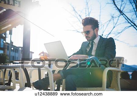 Stylish young businessman using laptop at sidewalk cafe View Large Photo Image Stock Photo - Stylish young businessman using laptop at sidewalk cafe. Fotosearch