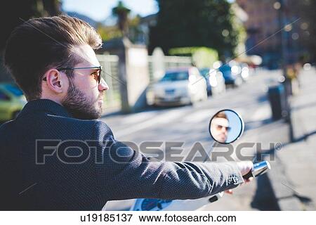 Stylish young man looking away from moped View Large Photo Image Stock Photo - Stylish young man looking away from moped. Fotosearch