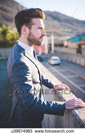 Stock Image - Stylish young man looking out from roadside wall. Fotosearch