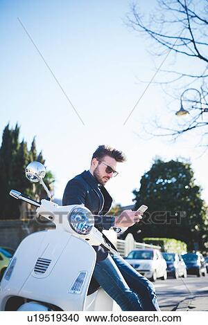 Stylish young man reading smartphone texts on moped View Large Photo Image Stock Image - Stylish young man reading smartphone texts on moped. Fotosearch