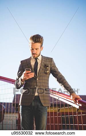 Stylish young man reading smartphone texts on footbridge View Large Photo Image Stock Image - Stylish young man reading smartphone texts on footbridge. Fotosearch