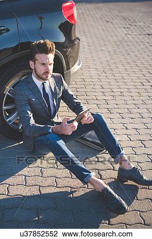 Stylish young man sitting leaning against car with digital tablet View Large Photo Image Stock Image - Stylish young man sitting leaning against car with digital tablet. Fotosearch