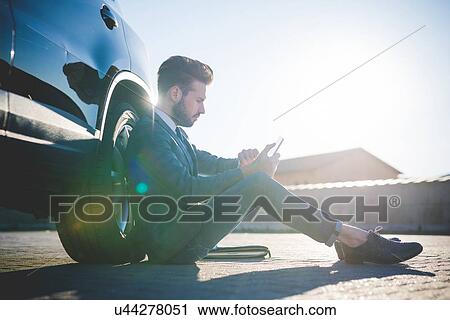 Stylish young man sitting leaning against car using digital tablet View Large Photo Image Stock Image - Stylish young man sitting leaning against car using digital tablet. Fotosearch