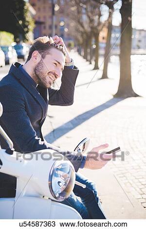 Stock Image - Stylish young man sitting on moped with smartphone. Fotosearch