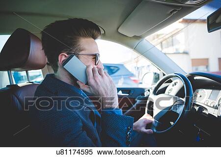 Stock Photography - Stylish young man talking on smartphone whilst driving car. Fotosearch