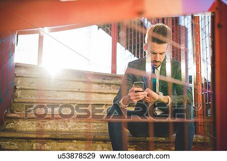 Stock Photo - Stylish young man with smartphone checking the time on footbridge. Fotosearch