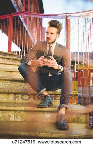 Stylish young man with smartphone sitting on footbridge stairs View Large Photo Image Stock Photo - Stylish young man with smartphone sitting on footbridge stairs. Fotosearch