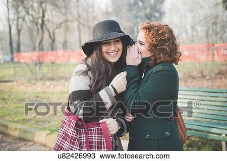 Two female adult friends whispering in park View Large Photo Image Stock Image - Two female adult friends whispering in park. Fotosearch