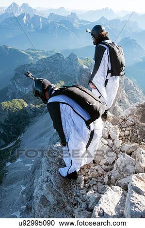 Stock Image - Two male BASE jumpers preparing to launch from mountain, Dolomites, Italy. Fotosearch