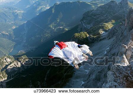 Stock Image - Two male BASE jumpers wingsuit flying from mountain, Dolomites, Italy. Fotosearch