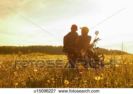 Stock Photo - Two young boys, sitting on motorbike, in field, rear view. Fotosearch