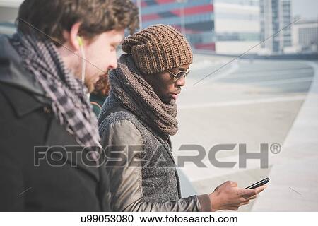 Stock Image - Two young men reading smartphone message on city street. Fotosearch