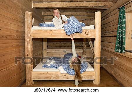 Picture - Two young women friends fooling around with pillows on bunk beds in log cabin. Fotosearch