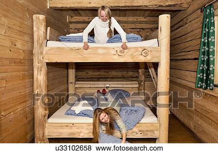 Stock Photo - Two young women friends fooling around on bunk beds in log cabin. Fotosearch