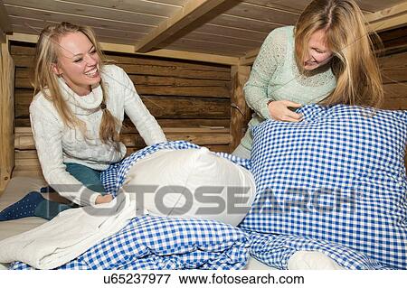 Stock Photo - Two young women friends having pillows fight in log cabin. Fotosearch