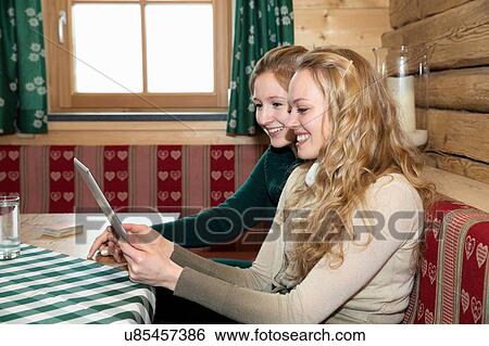 Stock Photograph - Two young women using digital tablet in log cabin. Fotosearch
