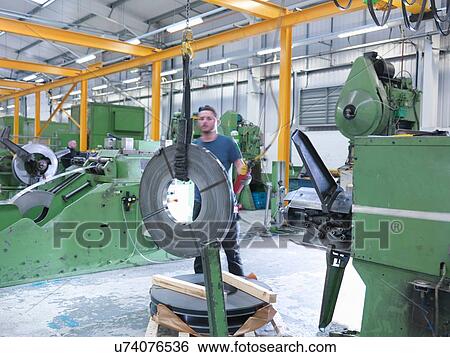 Stock Photograph - Worker loading rolls of metal into stamping machine in engineering factory. Fotosearch