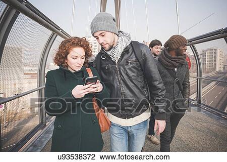 Stock Image - Young adult friends on footbridge reading smartphone text. Fotosearch