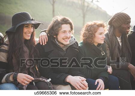 Young adult friends sitting on park bench View Large Photo Image Stock Photograph - Young adult friends sitting on park bench. Fotosearch