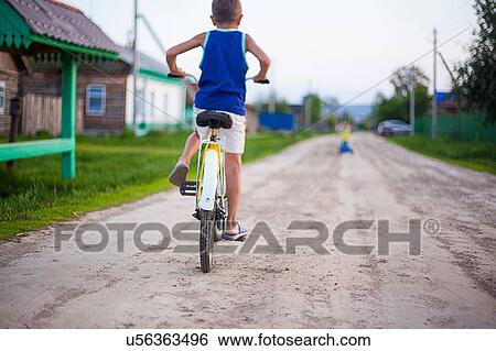 Stock Photograph - Young boy, riding bicycle along dirt road, rear view. Fotosearch