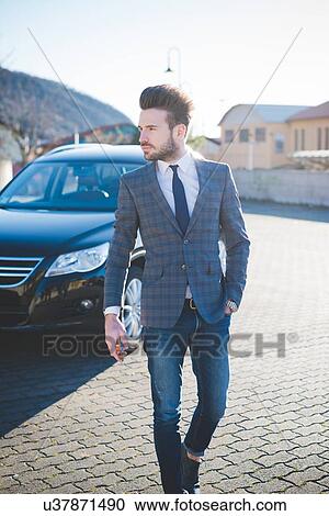 Stock Image - Young businessman walking across parking lot. Fotosearch