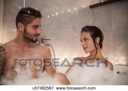 Stock Photo - Young couple gazing at each other in bubble bath. Fotosearch