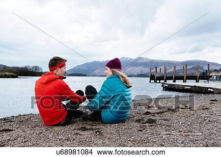Picture - Young couple hiking, sitting by waters edge, Derwent Water, Keswick, Lake District, Cumbria, United Kingdom. Fotosearch