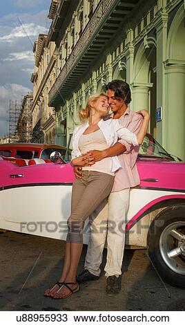 Stock Image - Young couple leaning against vintage convertible, Havana, Cuba. Fotosearch