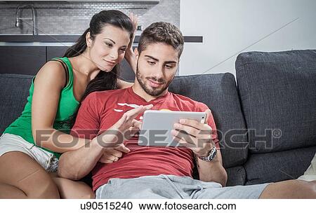Young couple on sofa using digital tablet View Large Photo Image Stock Image - Young couple on sofa using digital tablet. Fotosearch