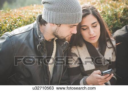 Young couple reading smartphone texts in park View Large Photo Image Stock Image - Young couple reading smartphone texts in park. Fotosearch