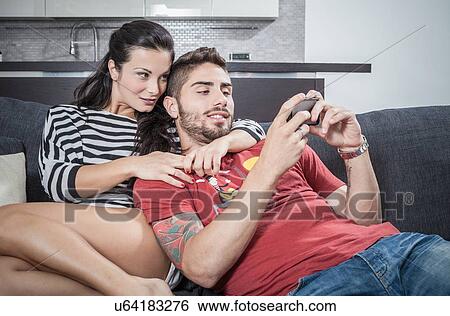Young couple reclining on sofa taking smartphone selfie View Large Photo Image Stock Photograph - Young couple reclining on sofa taking smartphone selfie. Fotosearch