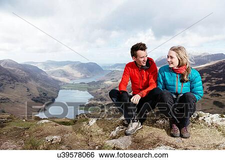 Stock Photograph - Young couple sitting on hilltop, Honister Slate Mine, Buttermere, Crummock Water, Keswick, Lake District, Cumbria, United Kingdom. Fotosearch