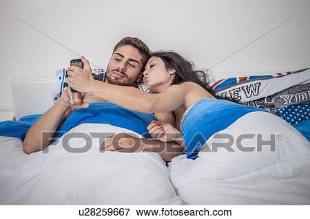 Young couple taking smartphone selfie in bed View Large Photo Image Stock Photo - Young couple taking smartphone selfie in bed. Fotosearch