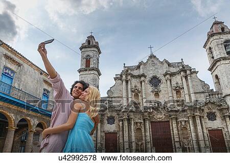 Stock Photo - Young couple taking smartphone selfie in the Plaza de la Cathedral of Havana, Cuba. Fotosearch