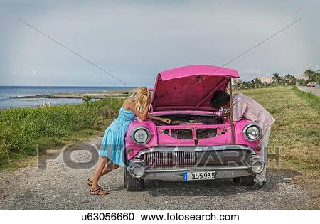 Stock Image - Young couple trying to fix a vintage convertible at coast, Havana, Cuba. Fotosearch