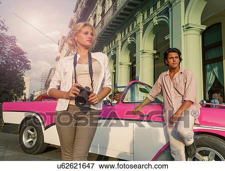 Stock Photo - Young couple with vintage convertible taking photographs, Havana, Cuba. Fotosearch