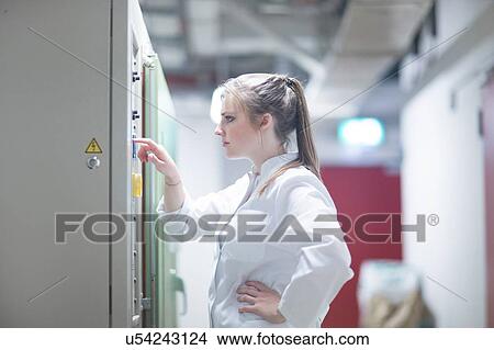 Picture - Young female scientist pressing button in technical room. Fotosearch