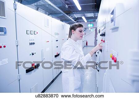 Stock Image - Young female scientist pressing button on machine control panel in technical room. Fotosearch