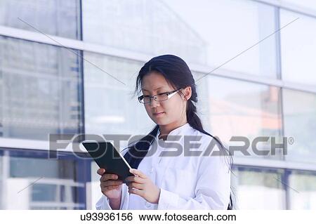 Stock Photograph - Young female scientist reading digital tablet outside laboratory. Fotosearch