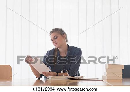 Picture - Young female student reading file index card at library desk. Fotosearch