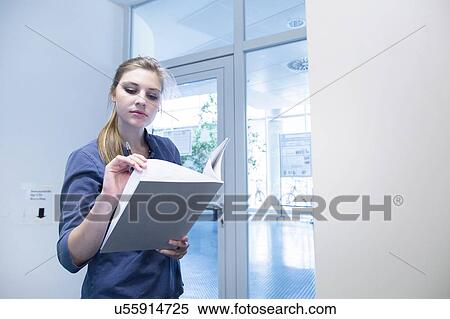 Stock Photography - Young female student reading textbook in library. Fotosearch
