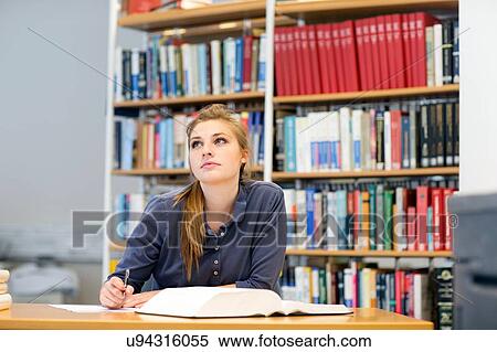 Stock Photography - Young female student reading textbook gazing up from library desk. Fotosearch
